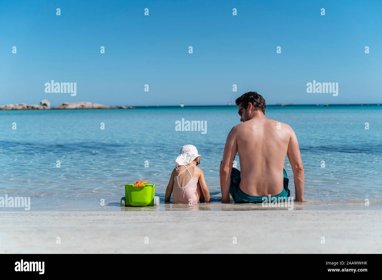 Rear view of father with daughter sitting in the sea Stock Photo