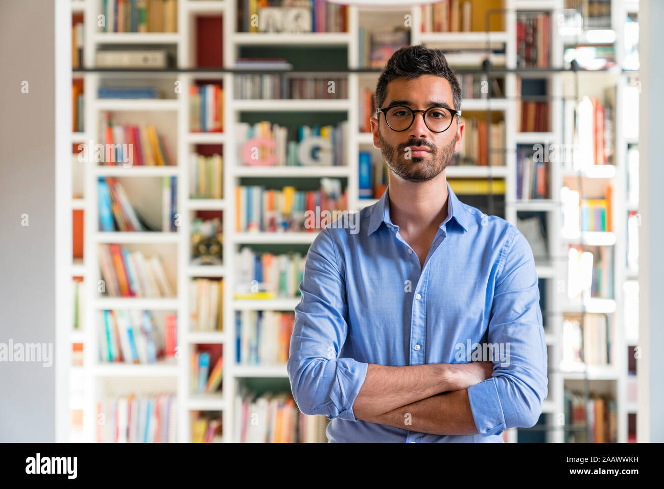 Portrait of bearded young man standing in front of bookshelves at home Stock Photo