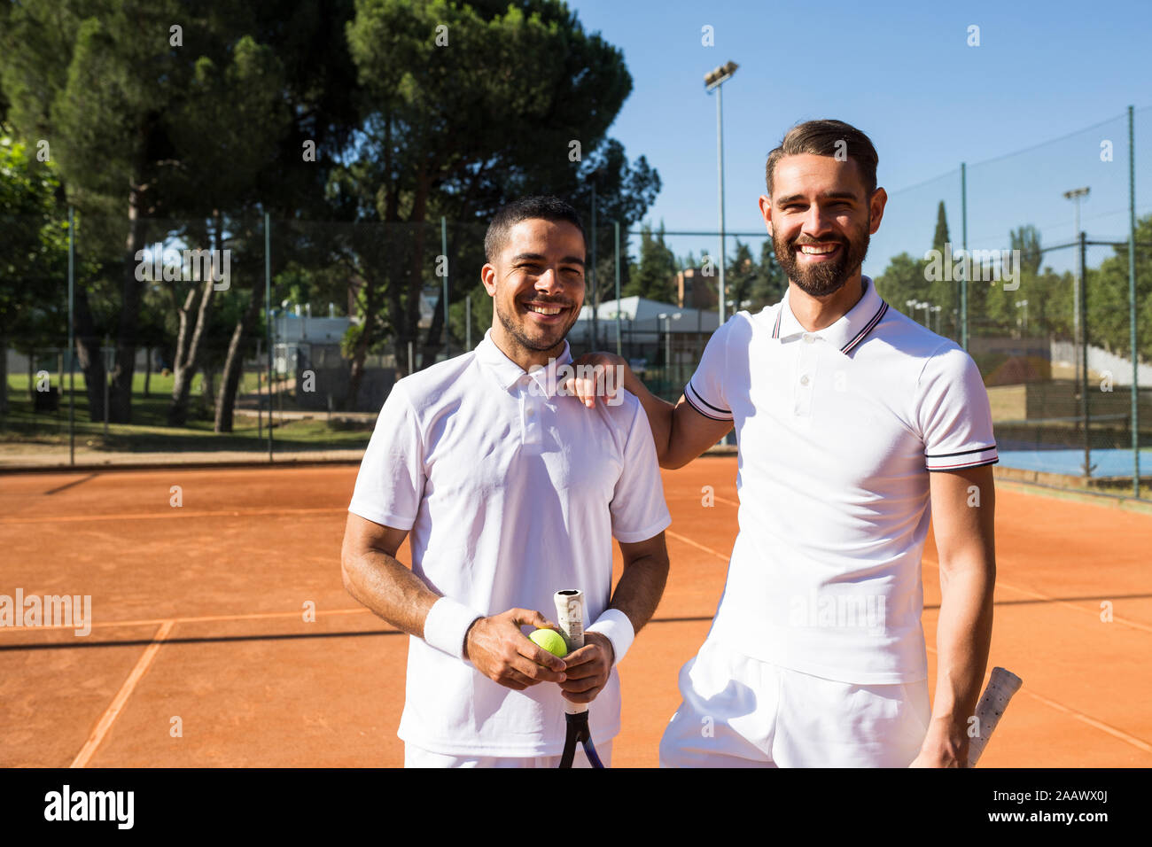 Two men in white sportswear holding rackets and smiling while standing ...