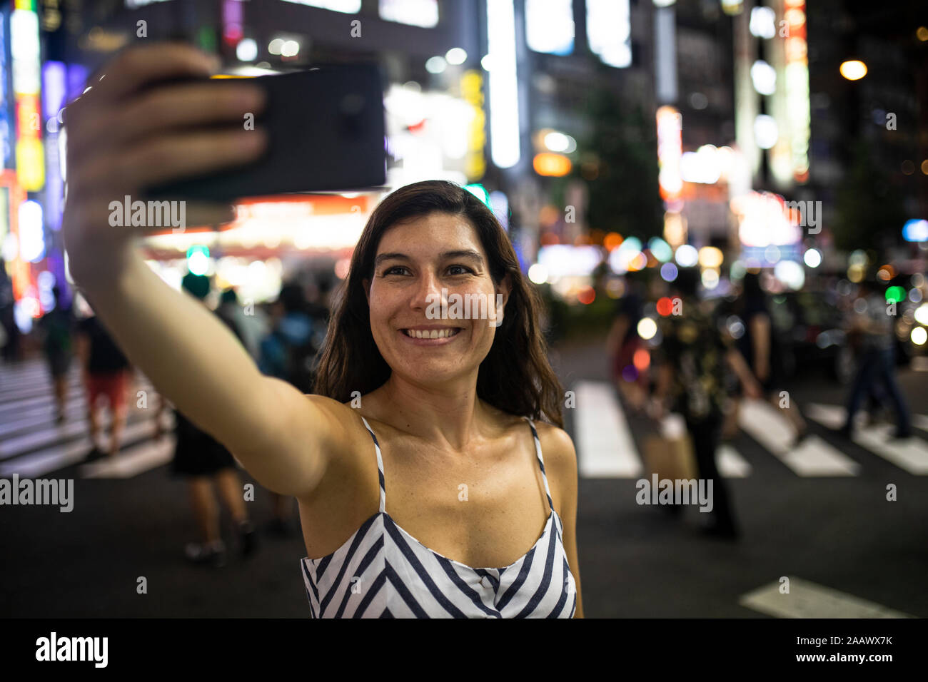 Young woman taking a selfie at night in the streets of Shinjuku, Tokio, Japan Stock Photo