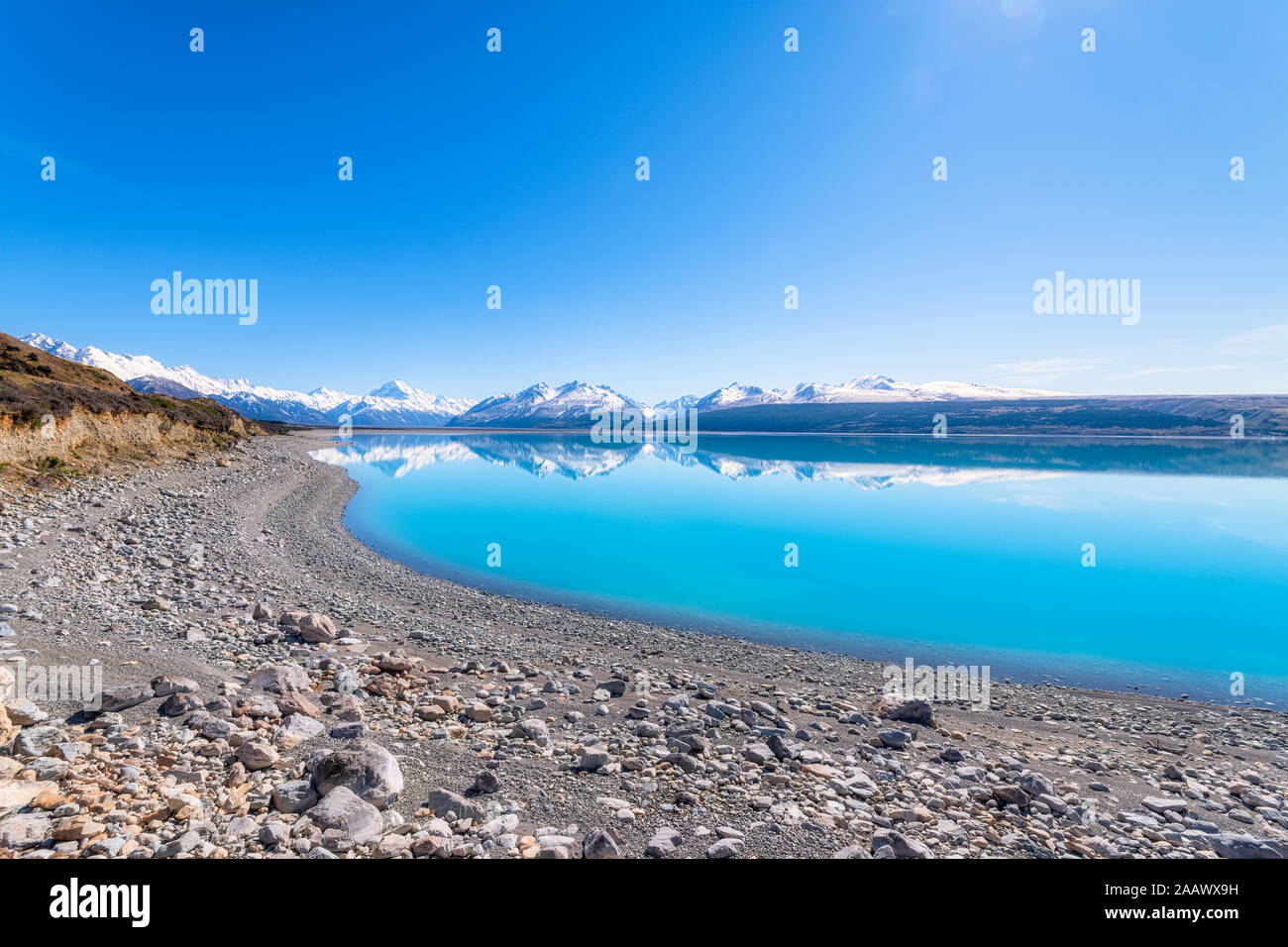 New Zealand, South Island, Clear sky over rocky shore of Lake Pukaki with mountains in background Stock Photo