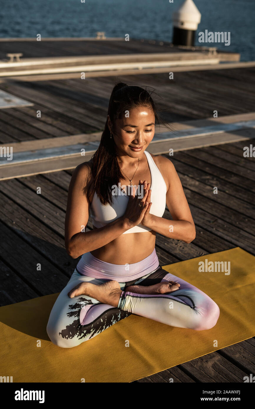 Asian woman practicing yoga on a pier at harbour at sunset, swan