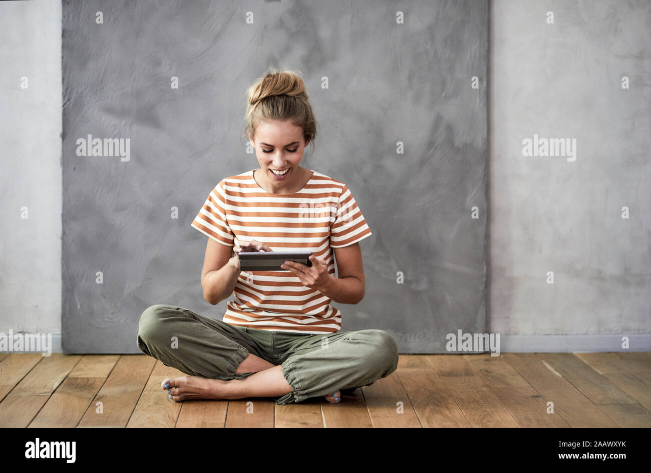 Smiling young woman sitting on the floor using a digital tablet Stock Photo