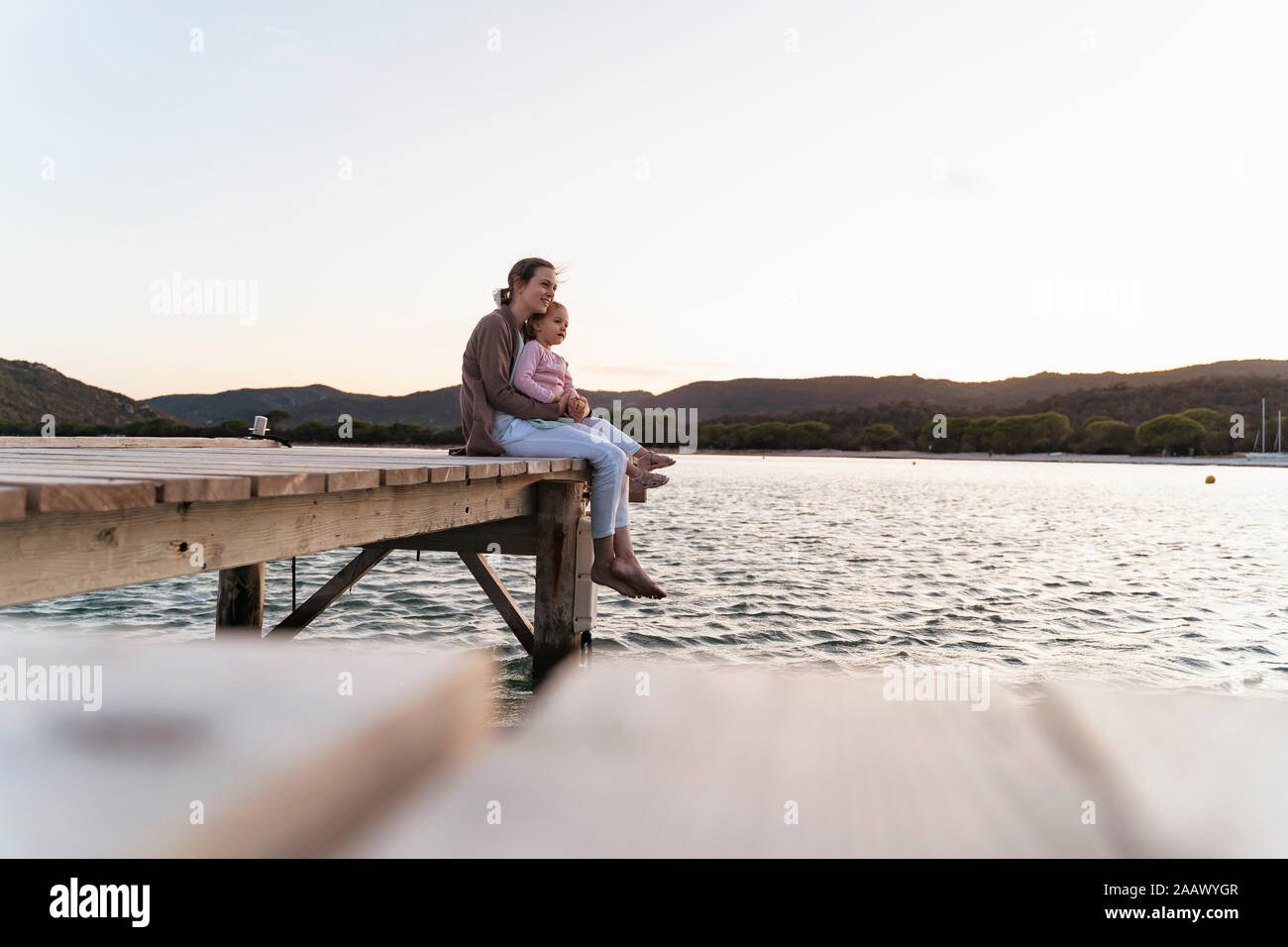 Mother with daughter sitting on a jetty at sunset Stock Photo