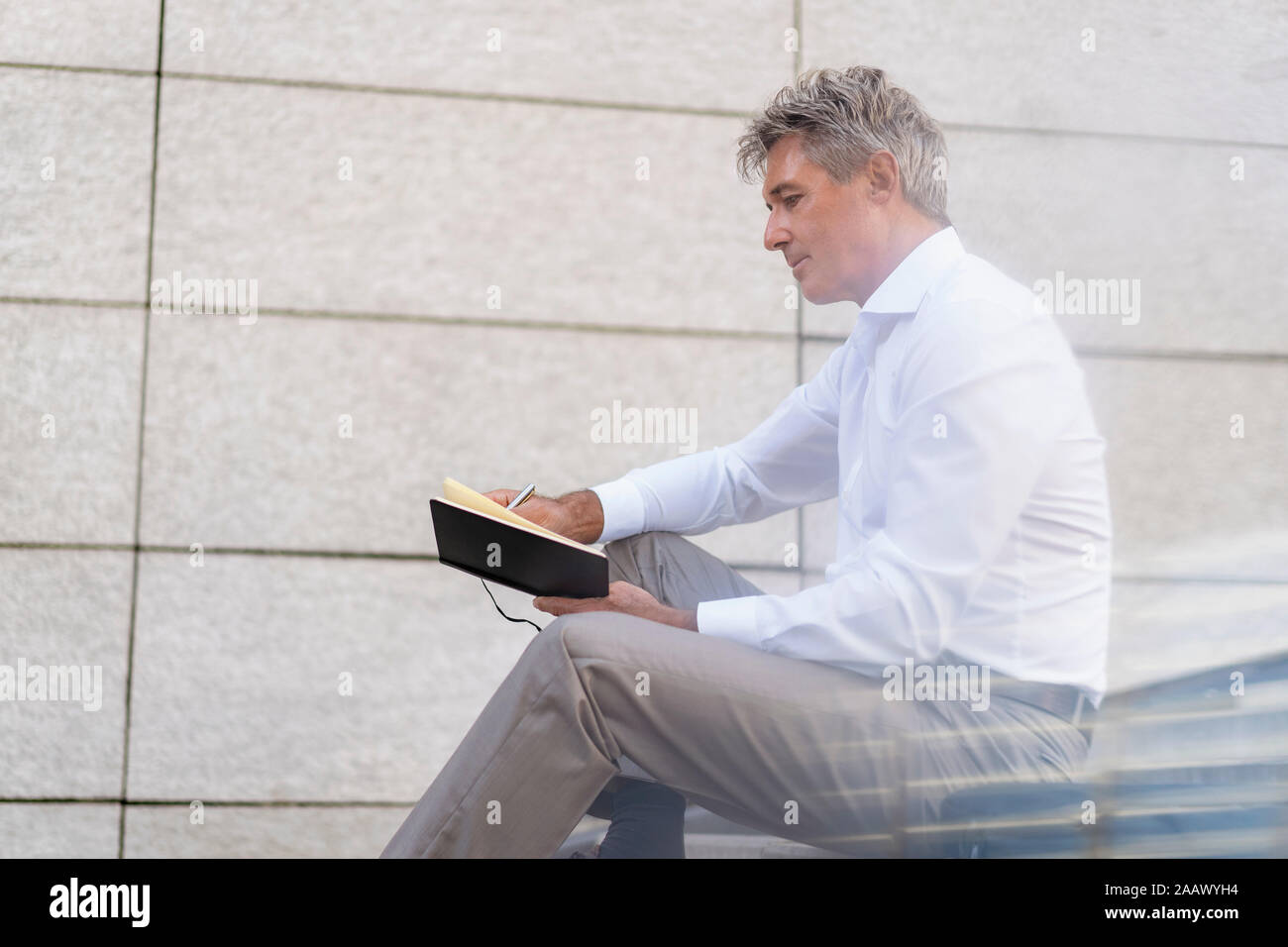 Mature businessman sitting on stairs looking at notebook Stock Photo