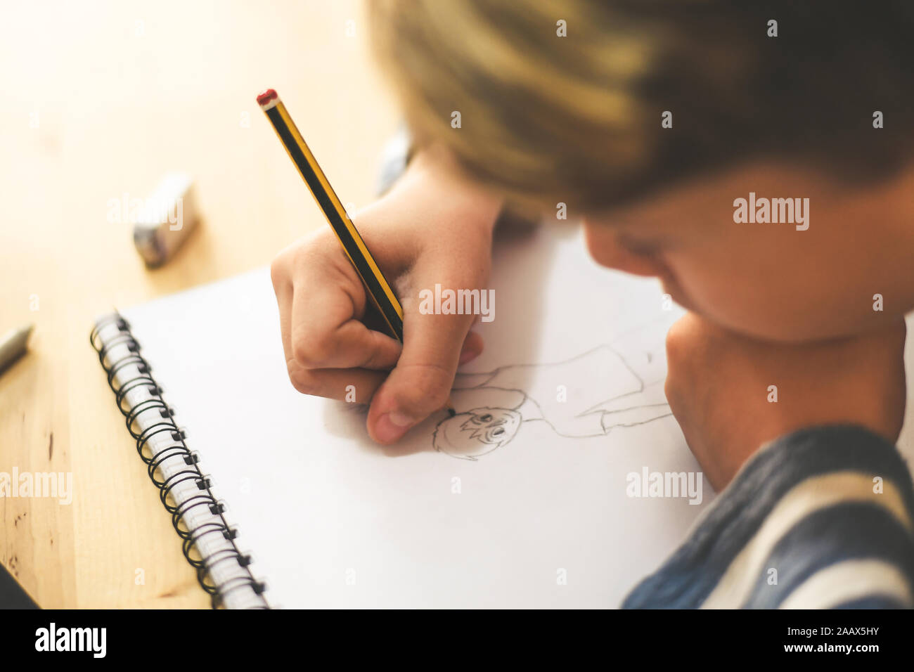 Close up view of student drawing with pencil. Boy doing homework writing on a paper. Kid hold a pencil and draw a manga at home. Teen drawing sitting Stock Photo