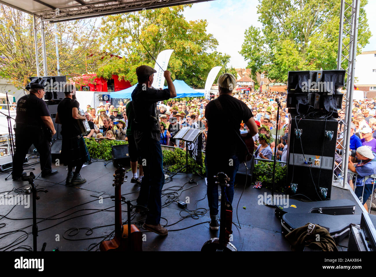 Faversham Hop Festival. Back of stage view of the French rock band 'Sur Les Docks' playing a concert in front of a packed crowd during a sunny day. Stock Photo