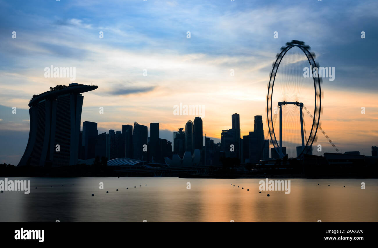 Stunning view of the silhouette of the skyline of Singapore with skyscrapers and a ferry wheel during a breathtaking sunset. Stock Photo