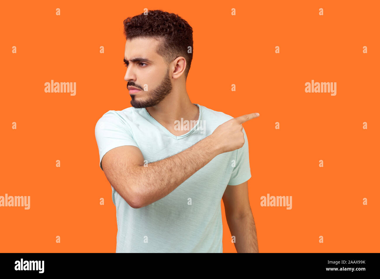 Get out! Portrait of annoyed brunette man with beard in white t-shirt looking aside and pointing finger another way, ordering to leave with bossy expr Stock Photo