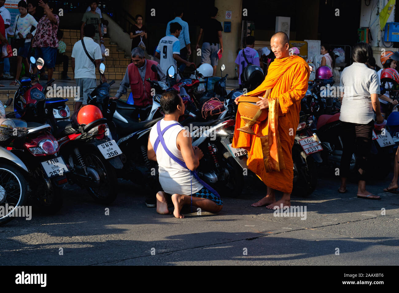 A Thai shopkeeper kneels in front of a Buddhist monk with his alms bowl, asking for his blessings; Phuket Town, Phuket, Thailand Stock Photo