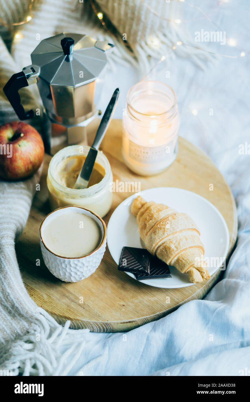 Cozy winter weekend breakfast, coffee and croissant on wooden tray in bed, vintage filter Stock Photo