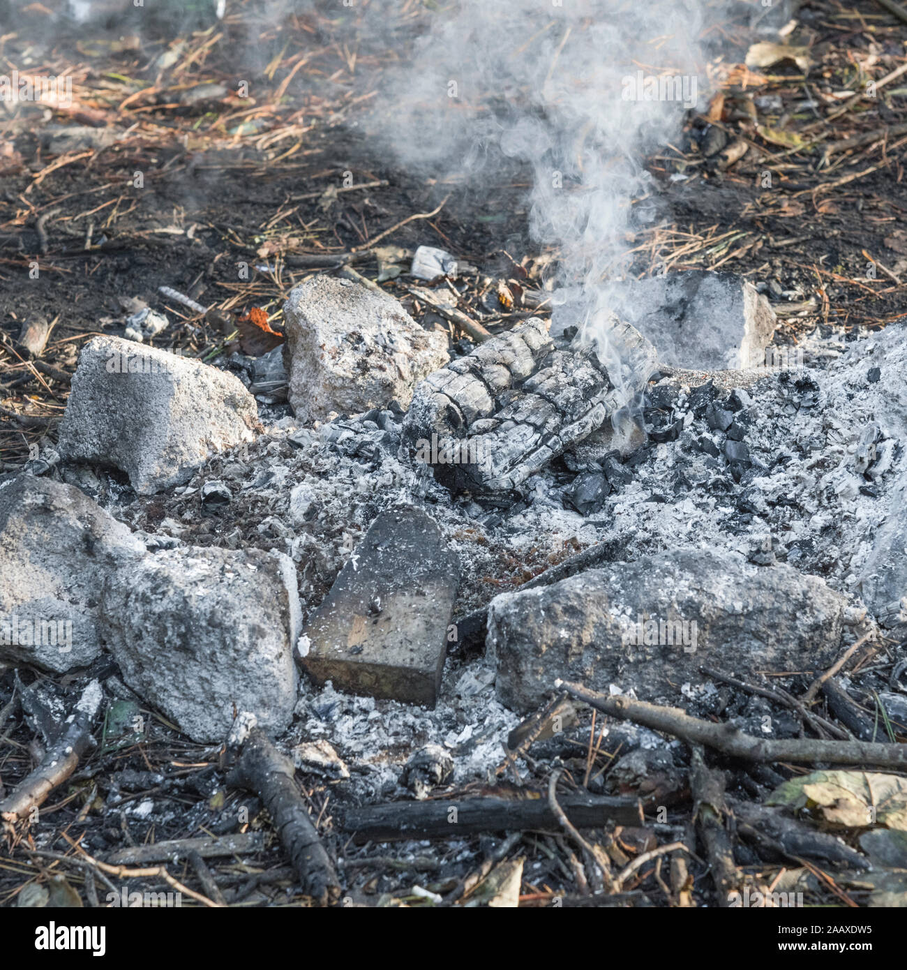 Smouldering wood ash remains from wood burning campfire set in a stone fire circle. Metaphor survival skills, camping outdoors, camp fire, bushcraft. Stock Photo