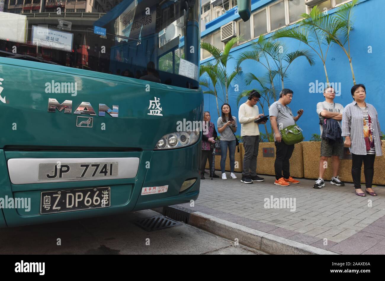 A bus with a Chinese registration plate stations next to people lining up at a polling station to vote in the Mong Kok District Council elections. Hong Kong held its district council election under a rare atmosphere of calm and peace after weeks of intense clashes at numerous universities between anti-government protesters and police which continue into its sixth month of demonstrations. Hong Kong held its district council election under a rare atmosphere of calm and peace after weeks of intense clashes at numerous universities between anti-government protesters and police which continue into Stock Photo