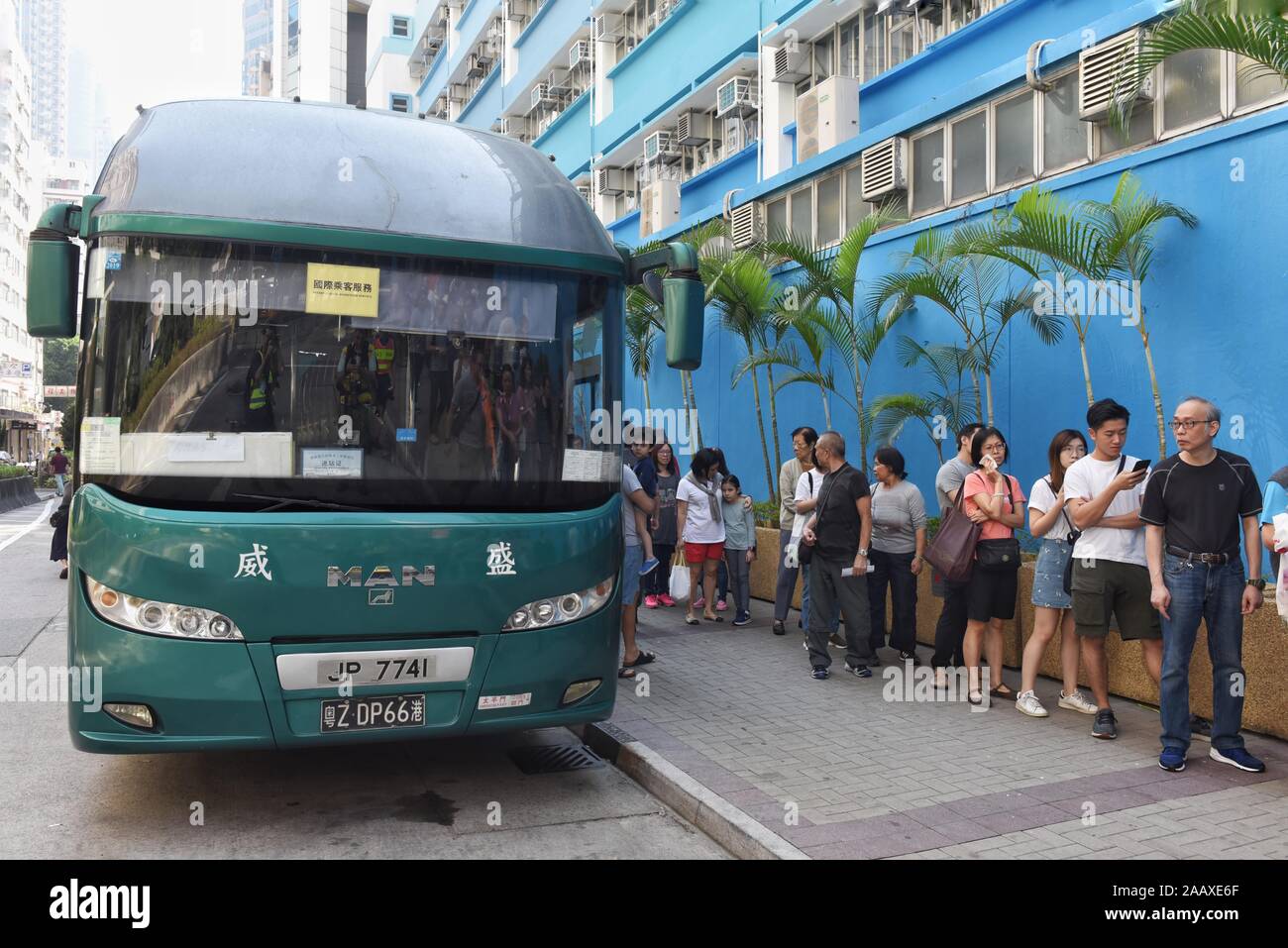 A bus with a Chinese registration plate stations next to people lining up at a polling station to vote in the Mong Kok District Council elections. Hong Kong held its district council election under a rare atmosphere of calm and peace after weeks of intense clashes at numerous universities between anti-government protesters and police which continue into its sixth month of demonstrations. Stock Photo