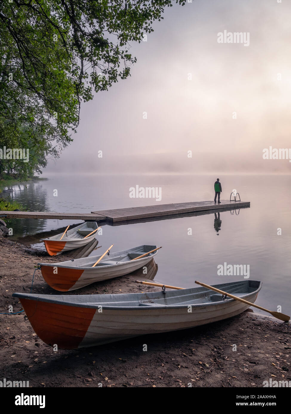 Tranquil beauty morning with row boat and pier at misty summer sunrise in idyllic beach Finland Stock Photo