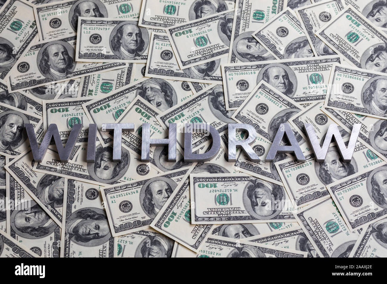 The word WITHDRAW laid with aluminium letters on the US dollar banknotes background - with selective focus and straight composition. Stock Photo