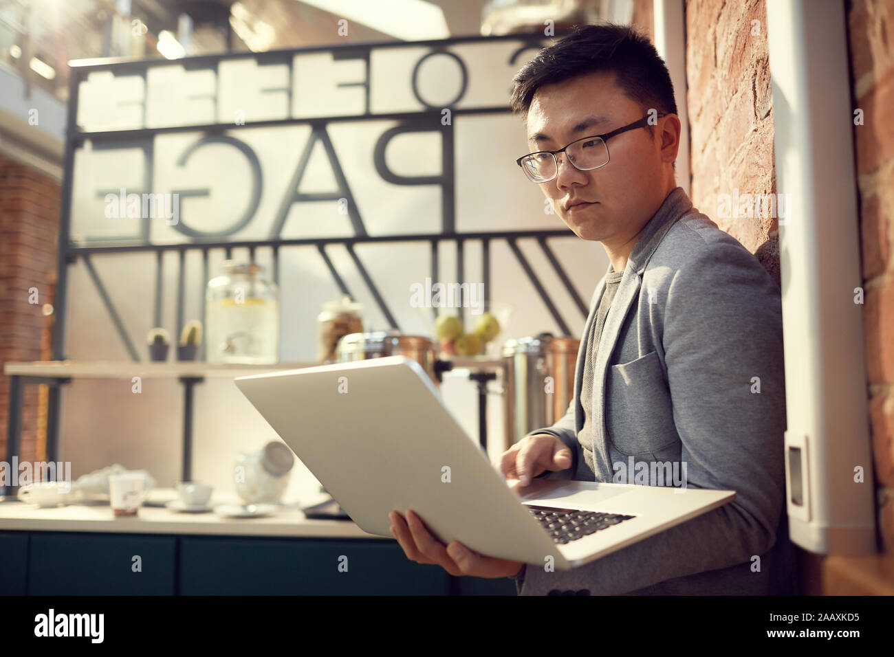 Side view portrait of modern Asian entrepreneur using laptop standing ...