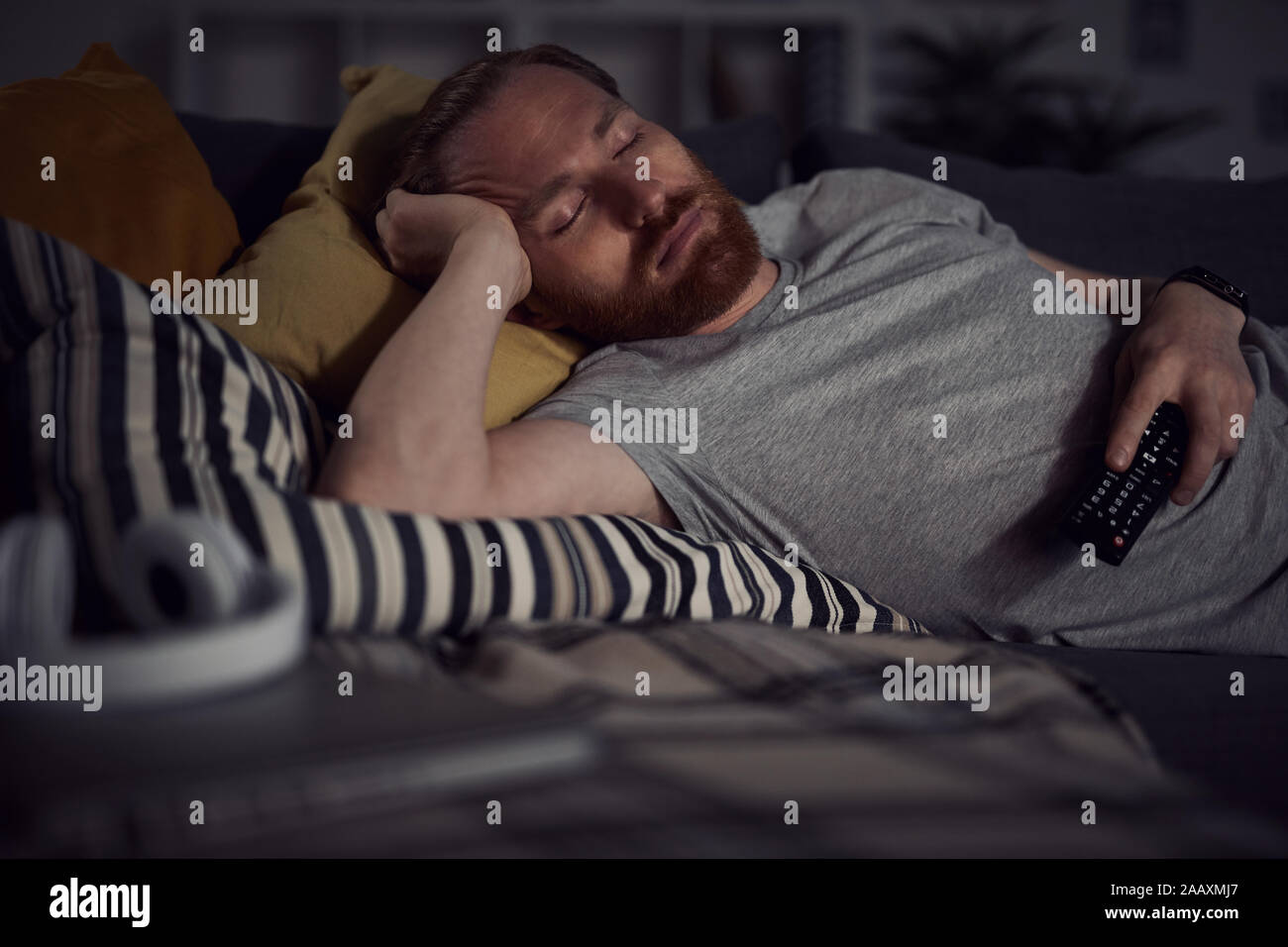 Portrait of bearded adult man sleeping on sofa while watching TV at night, copy space Stock Photo