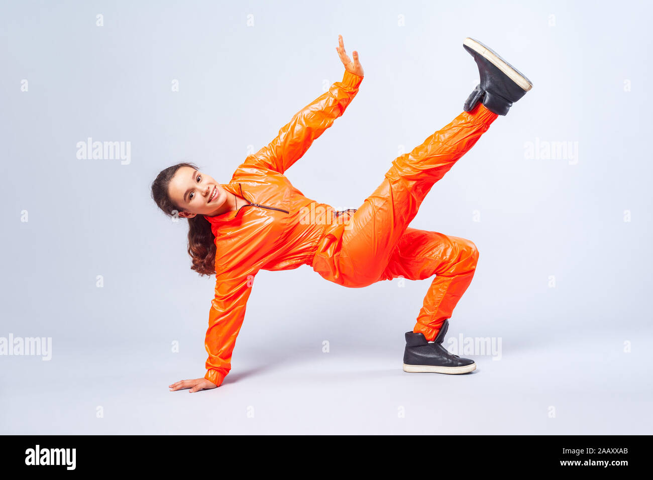 Full length image of vivid happy teenage girl with brunette hair wearing bright orange jumpsuit dancing hip-hop, showing move with handstand, hobby ac Stock Photo