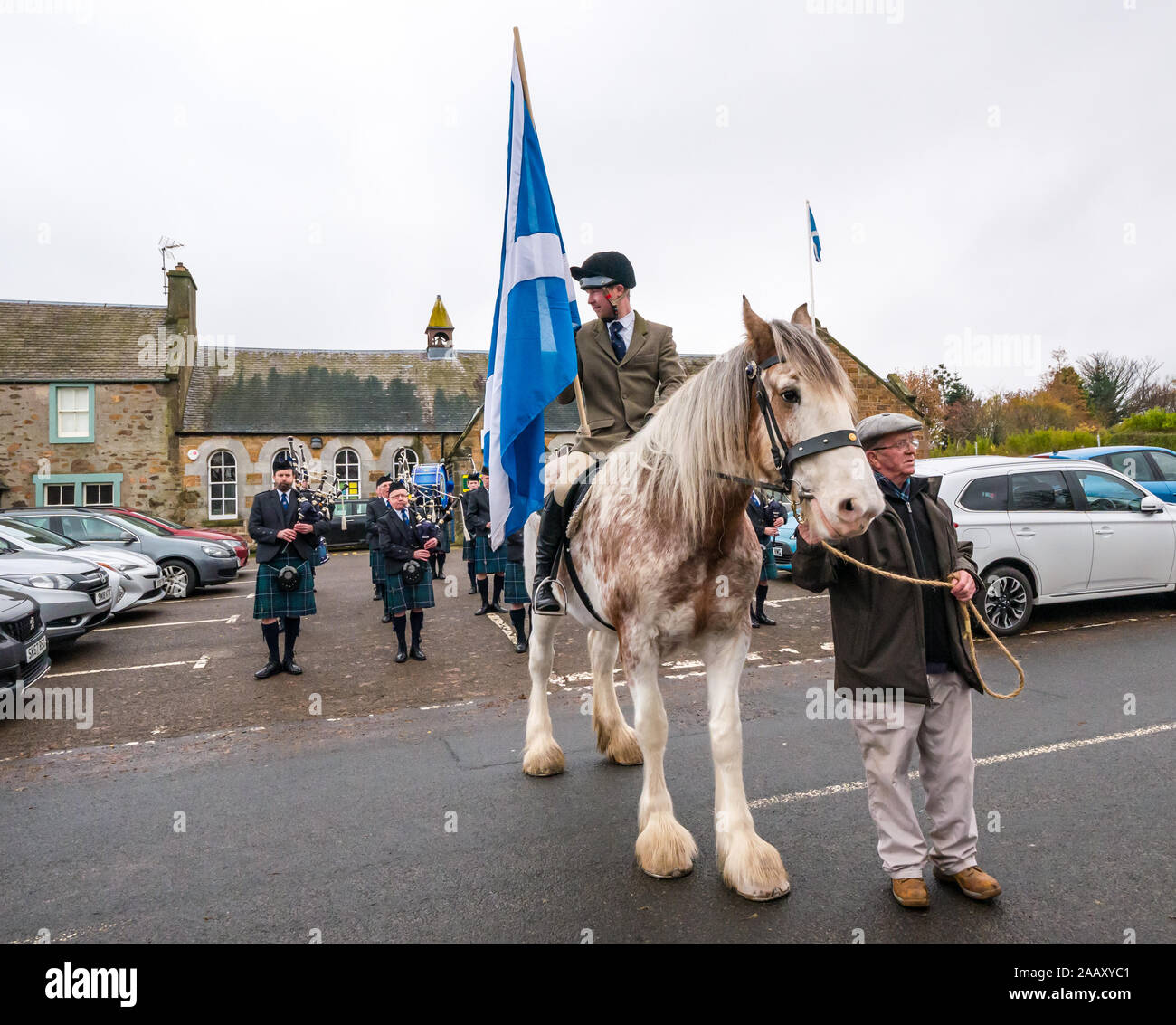 Athelstaneford, East Lothian, Scotland, UK. 24 November 2019. Saltire Festival: The first day of the annual festival to mark St Andrew’s Day takes place in the birthplace of the Scottish national flag where the saltire appeared in the sky as a good omen when the Picts & Scots defeated the Saxons led by Athelstan. Pictured: Craig Donnelly on a Strawberry Roan Clydesdale mare with groom/owner Arthur Greenan with Haddington Pipe Band Stock Photo