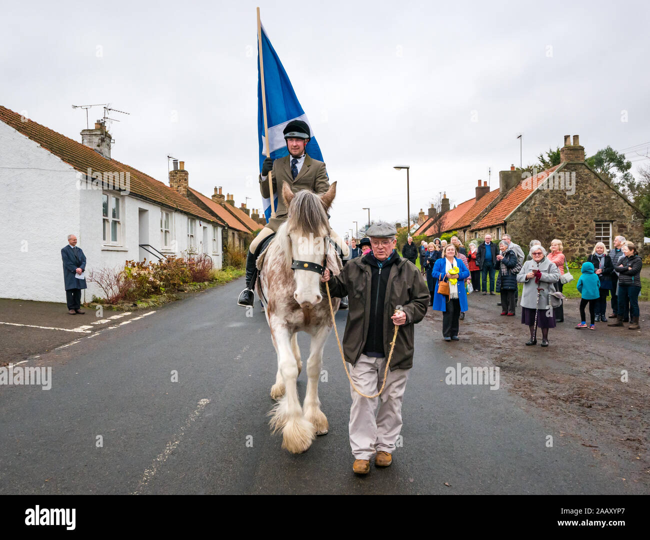 Athelstaneford, East Lothian, Scotland, UK. 24 November 2019. Saltire Festival: The first day of the annual festival to mark St Andrew’s Day takes place in the birthplace of the Scottish national flag where the saltire appeared in the sky as a good omen when the Picts & Scots defeated the Saxons led by Athelstan. Pictured: Craig Donnelly on a Strawberry Roan Clydesdale mare with groom/owner Arthur Greenan with villagers parading along the main street Stock Photo