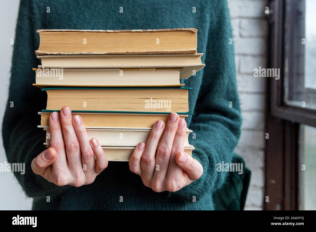 Girl hold stack of books. Women in green sweater hold old textbooks for research Stock Photo