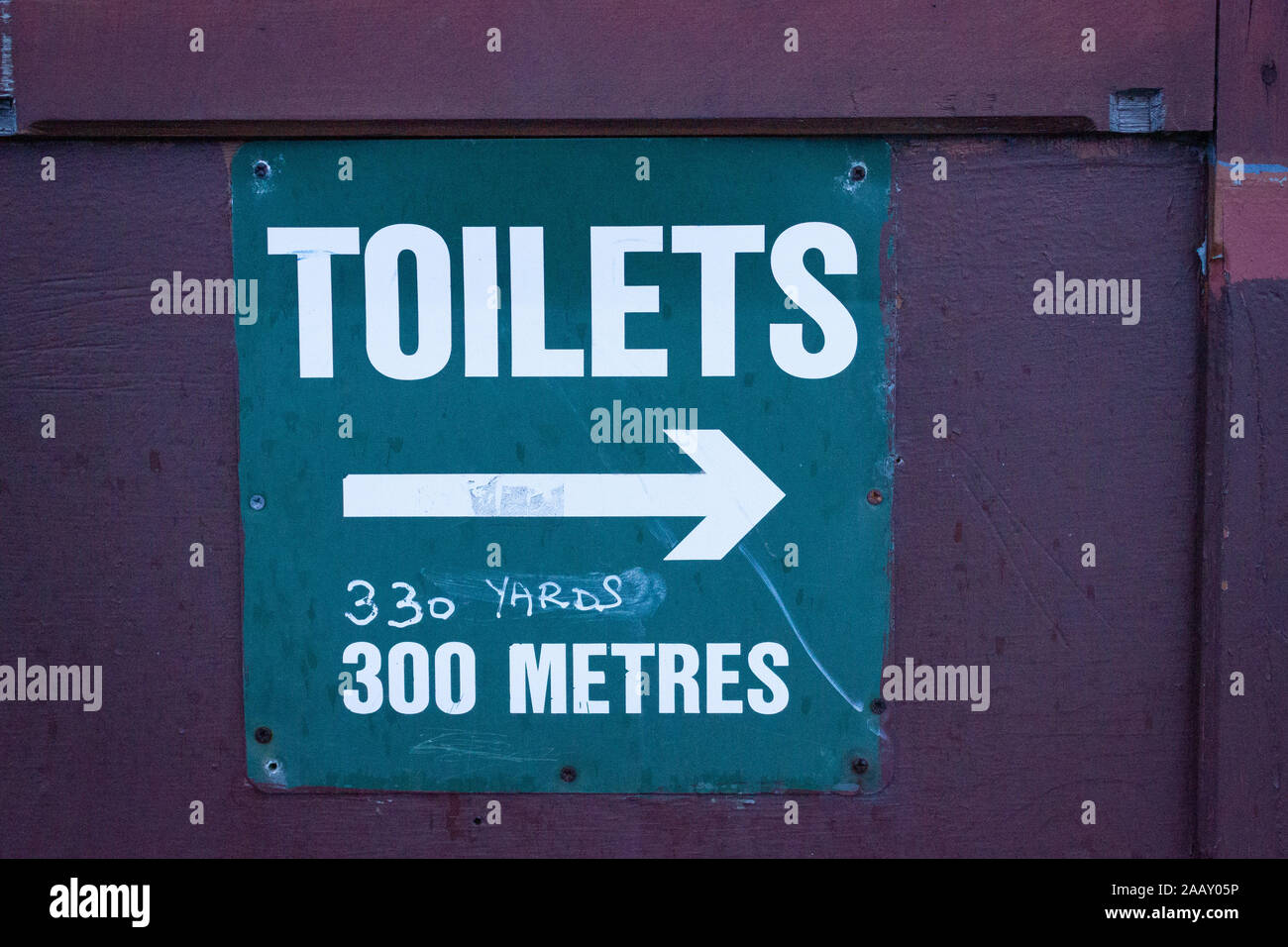 An old information sign. The toilets are that way, in metres and yards (handwritten), in Dartmouth, Devon, England Stock Photo