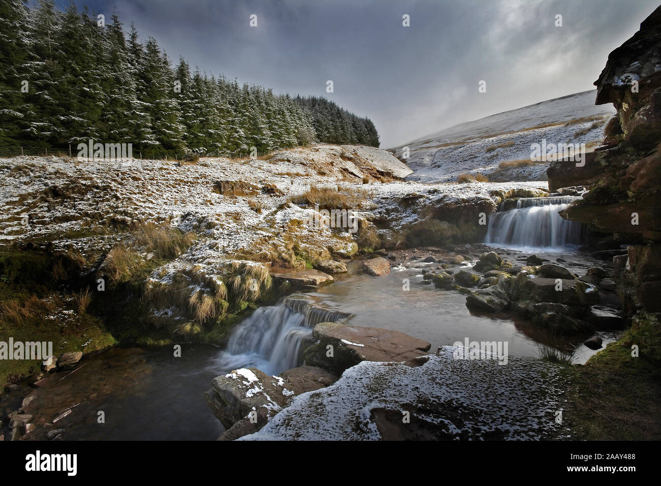 Mountain stream with small waterfalls in winter snow and dramatic sky Stock Photo