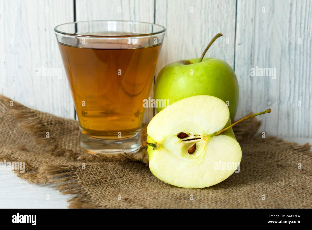 A glass of apple juice and a green apple on a white wooden background. Stock Photo
