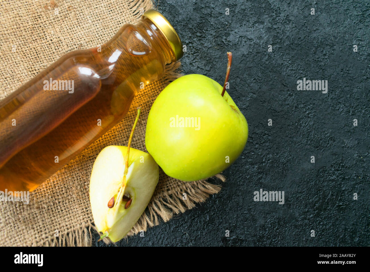 Apple juice in a bottle and a green apple on a black background. Flat lay. Copy space. Stock Photo