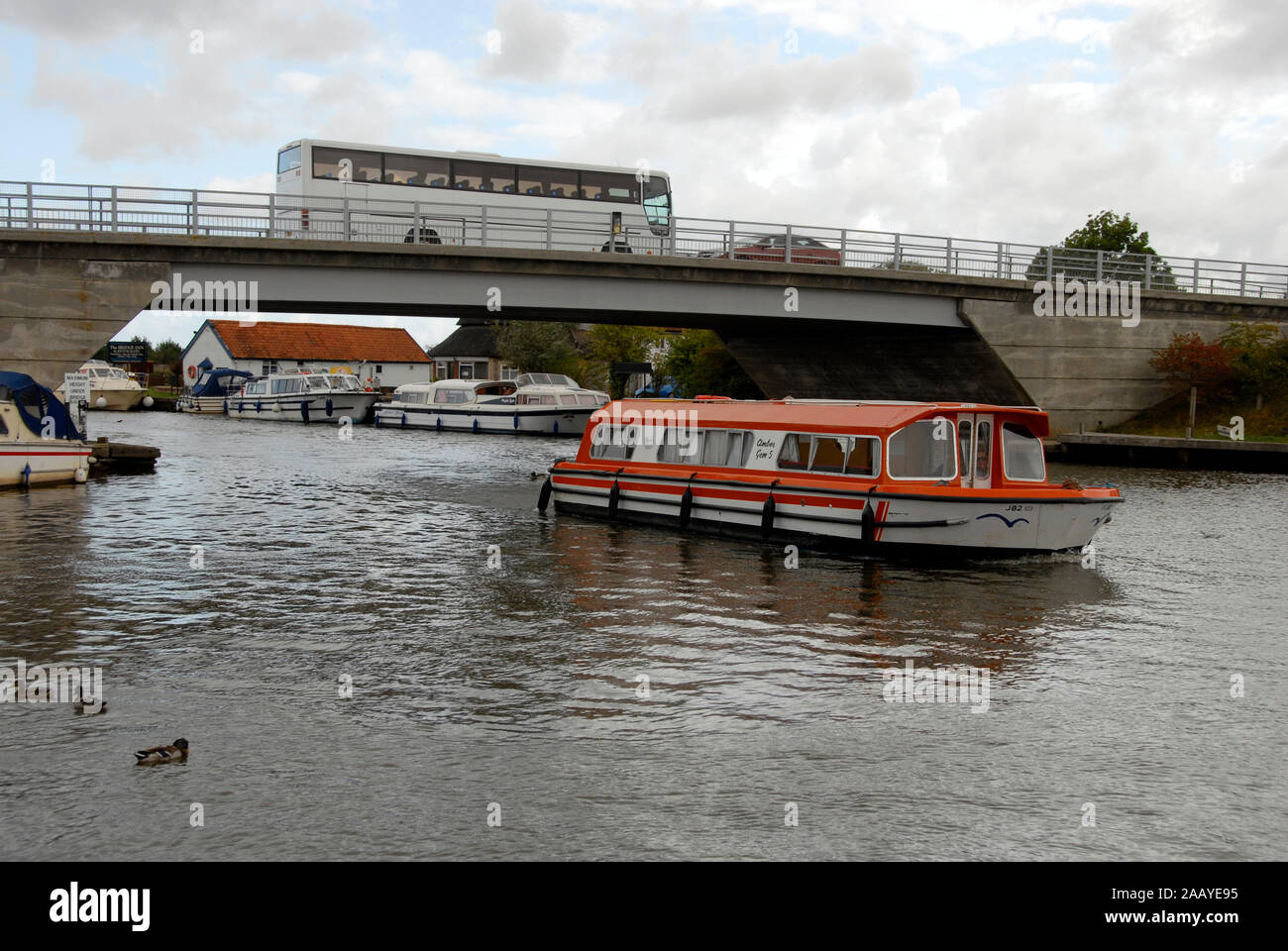 Motor cruiser passing under Acle bridge over the river Bure, Norfolk Broads, England, with coach passing over Stock Photo