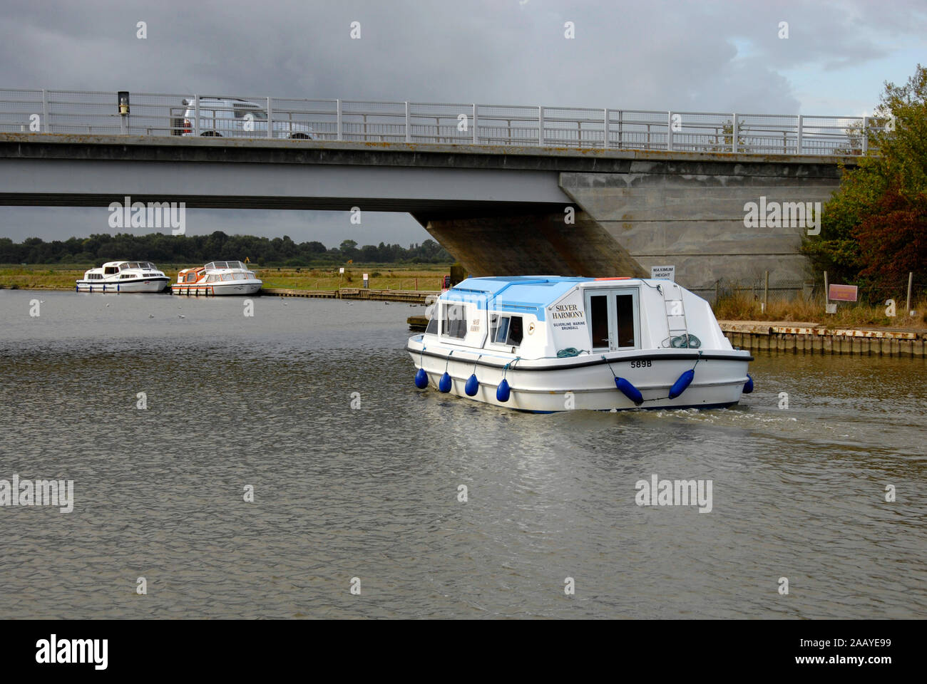 Motor cruiser passing under Acle bridge over the river Bure, Norfolk Broads, England, with car passing over Stock Photo