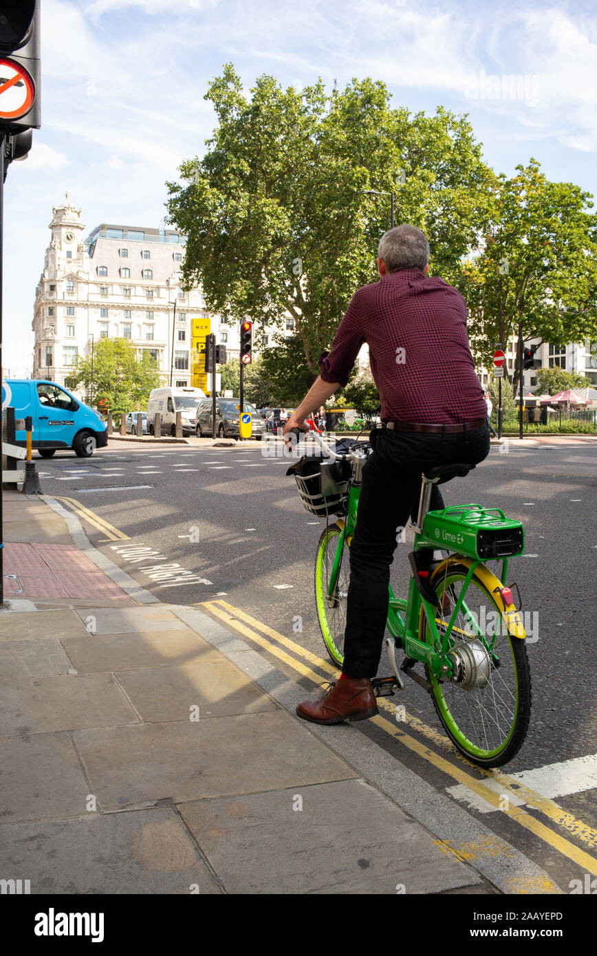 A single cyclist waits at the traffic lights of the junction of City Road and Chiswell Street London on a Lime electric rental bike. Stock Photo