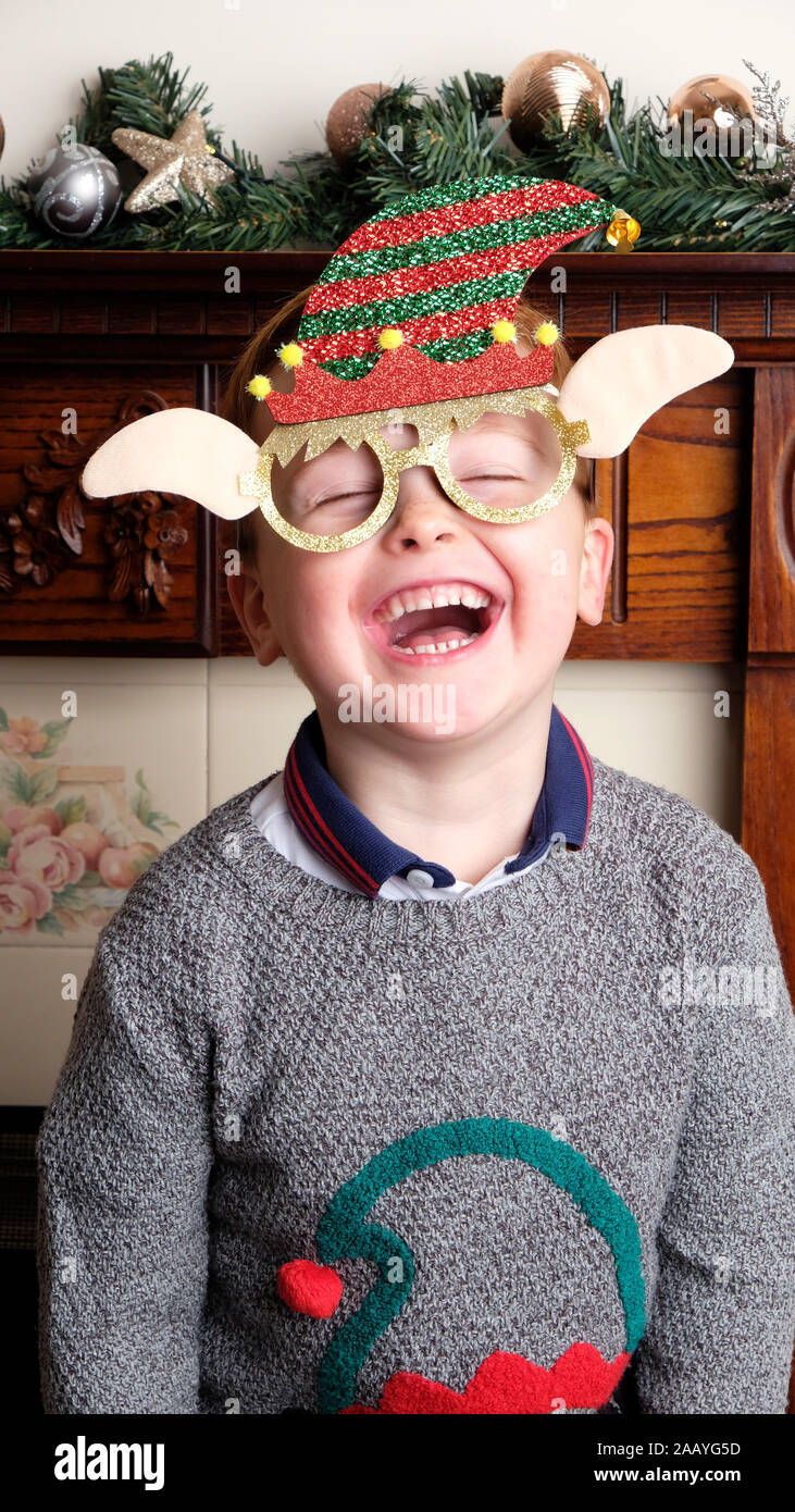 A young boy wearing a festive Christmas mask and smiling at the camera. There's a festive background to the shot with baubles and tinsel Stock Photo
