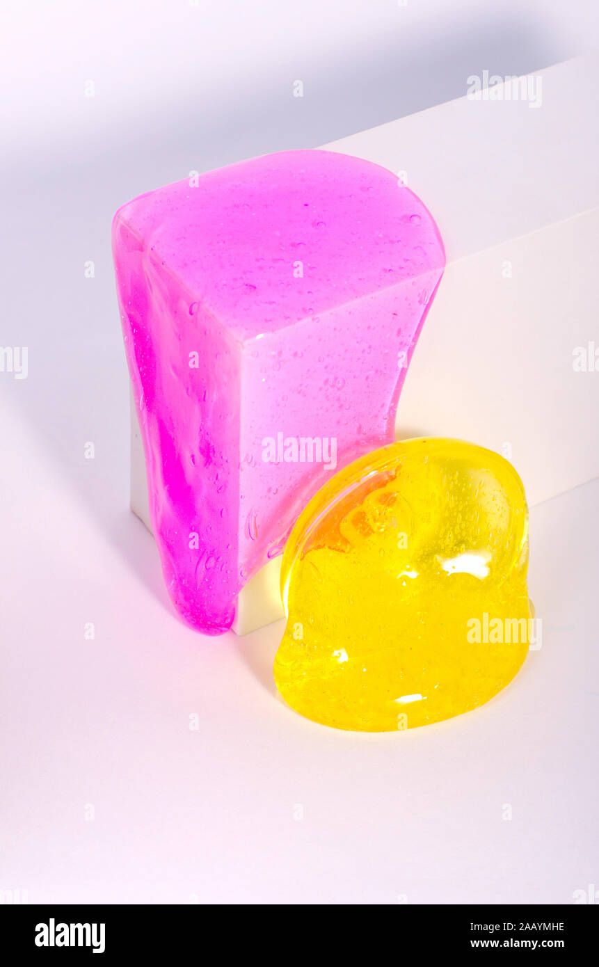 Slime, bright pink and yellow elastic toys flow down of white box, against white background. Stock Photo