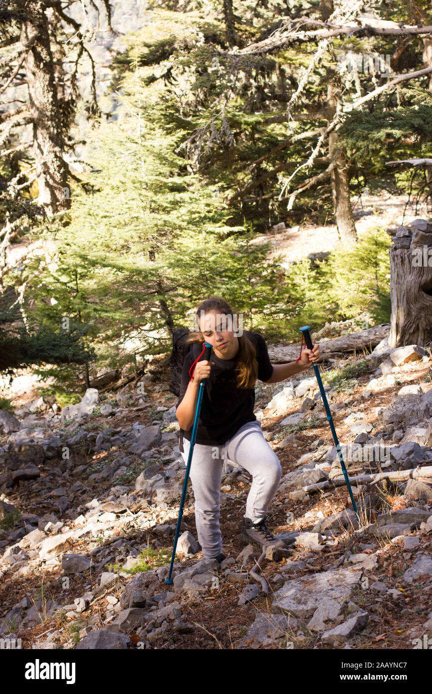 Young teenager girl with trekking poles and backpack in the forest