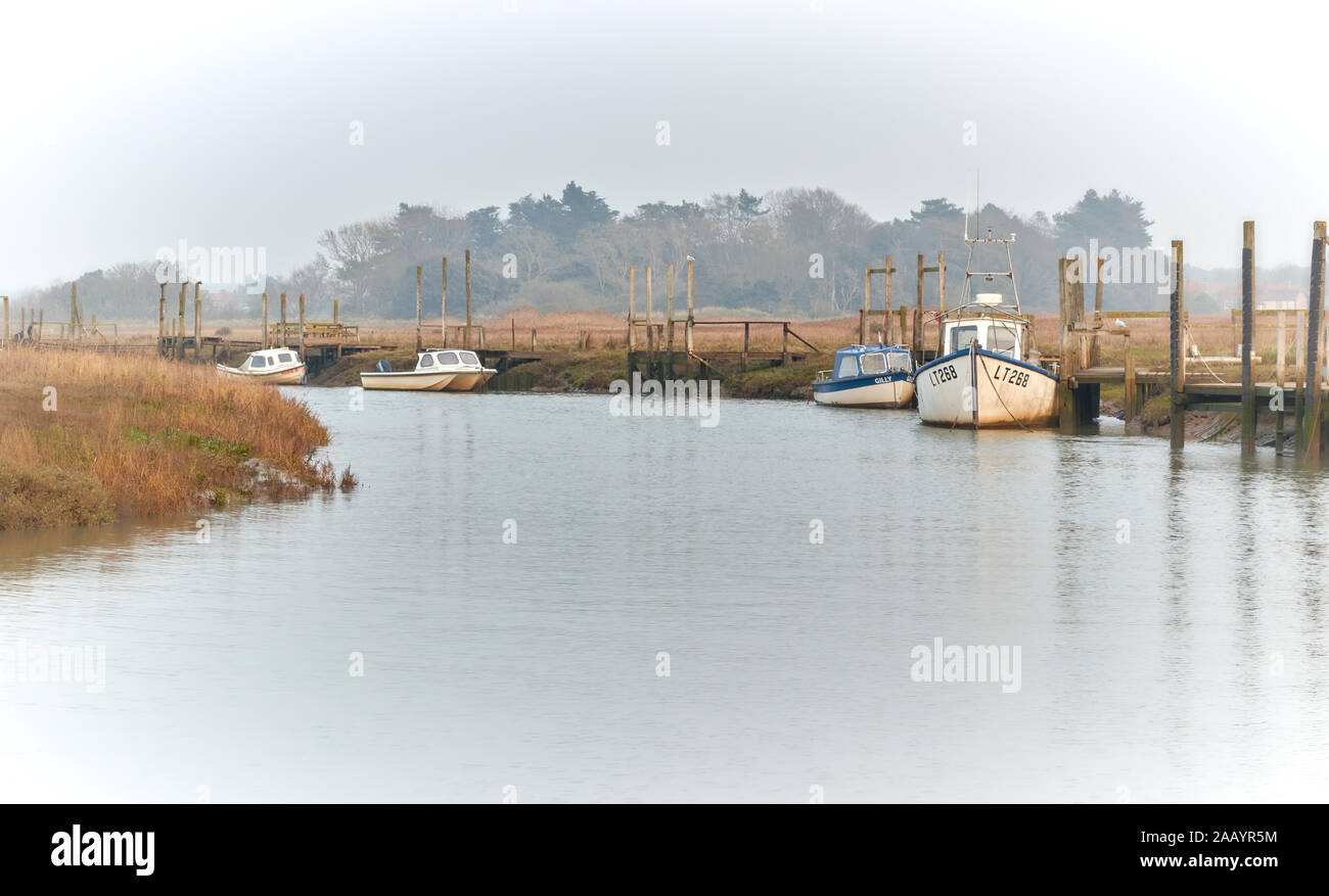 Small traditional fishing boats moored along an inlet at Thornham Old Harbour on the North Norfolk Coast in the hazy evening sun Stock Photo
