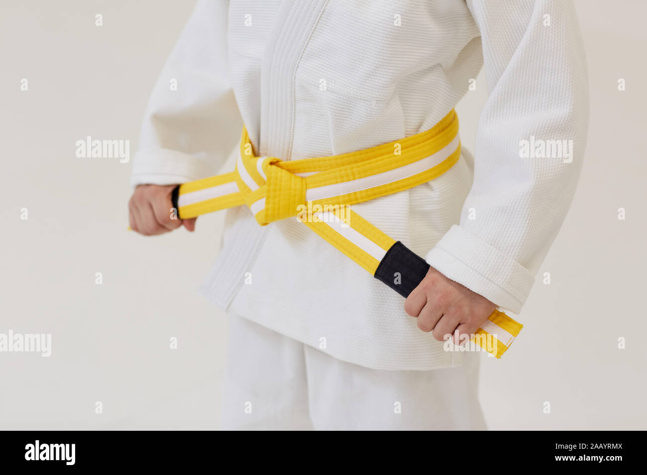 Close-up of young judoist standing in white kimono and holding yellow belt Stock Photo