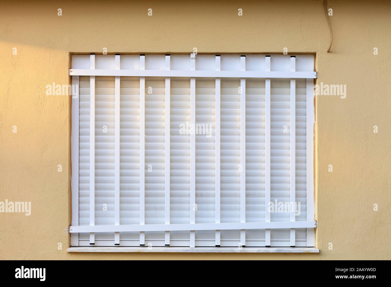 White metal shutters on the window of the facade of the house are closed with a white metal grill. Stock Photo