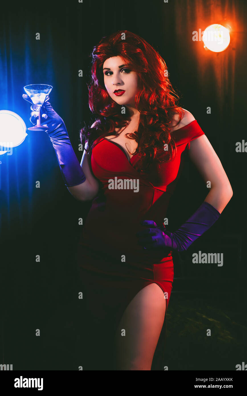 Glamorous woman in long red dress and purple evening gloves holding a cocktail drink Stock Photo