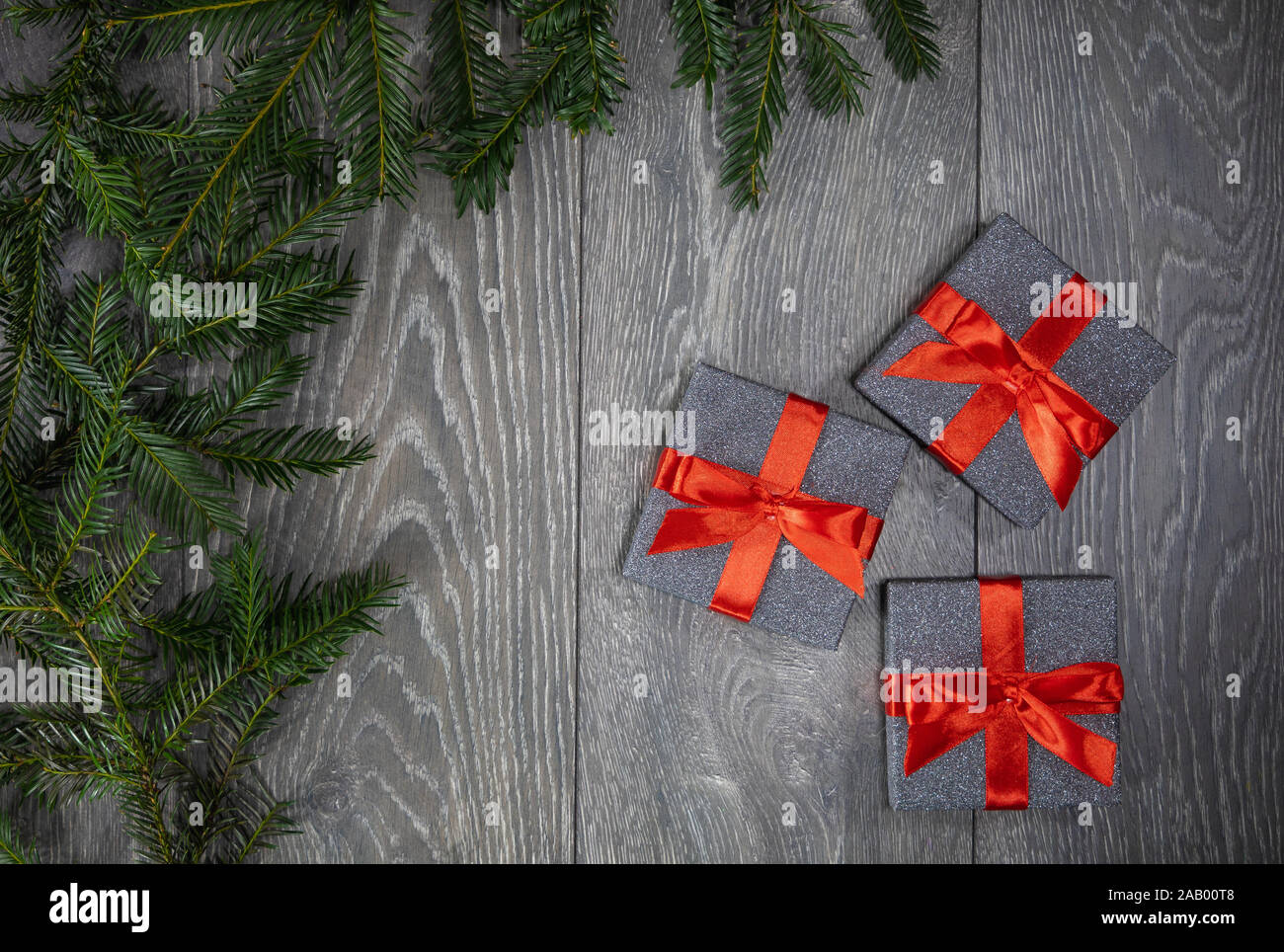 Three Christmas gifts boxes on a grey wooden floor background and the branch's of a Christmas tree bordering the left frame of photograph Stock Photo