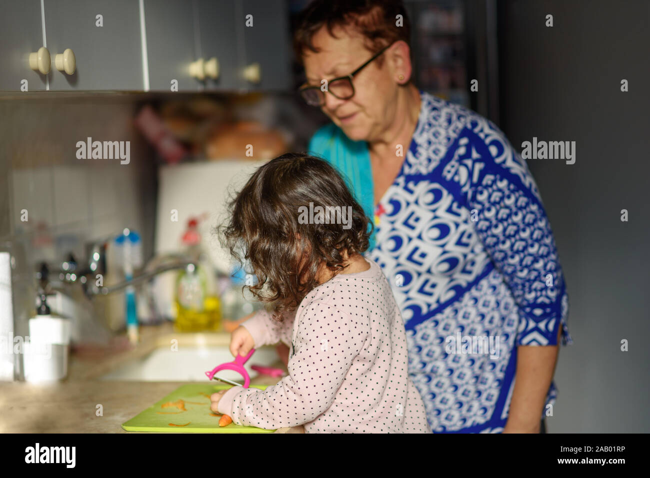https://c8.alamy.com/comp/2AB01RP/little-cute-baby-toddler-girl-with-grandmother-in-the-kitchen-peeling-carrots-with-carrot-peeler-on-chopping-board-child-help-at-home-cooking-with-kids-healthy-food-family-love-2AB01RP.jpg