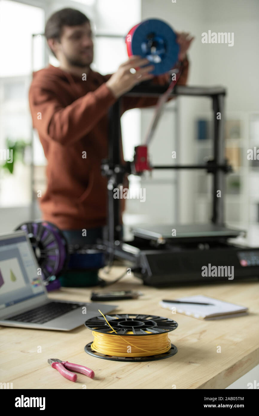 Spool with yellow filament and nippers on workplace of creative designer putting new threads in 3d printer Stock Photo