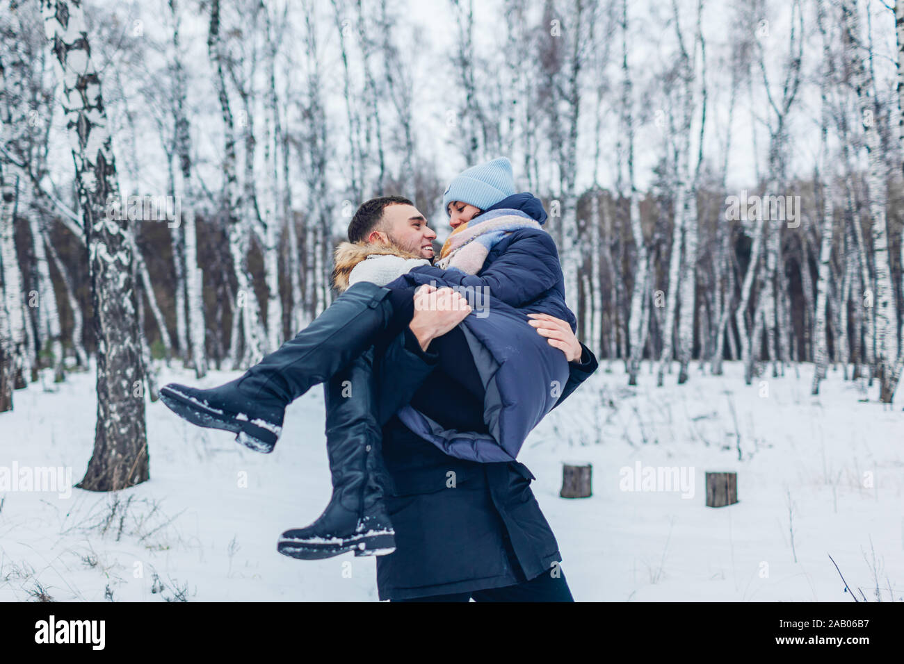 Man carrying his girlfriend on hands in winter forest. People having fun outdoors. Couple relaxing Stock Photo