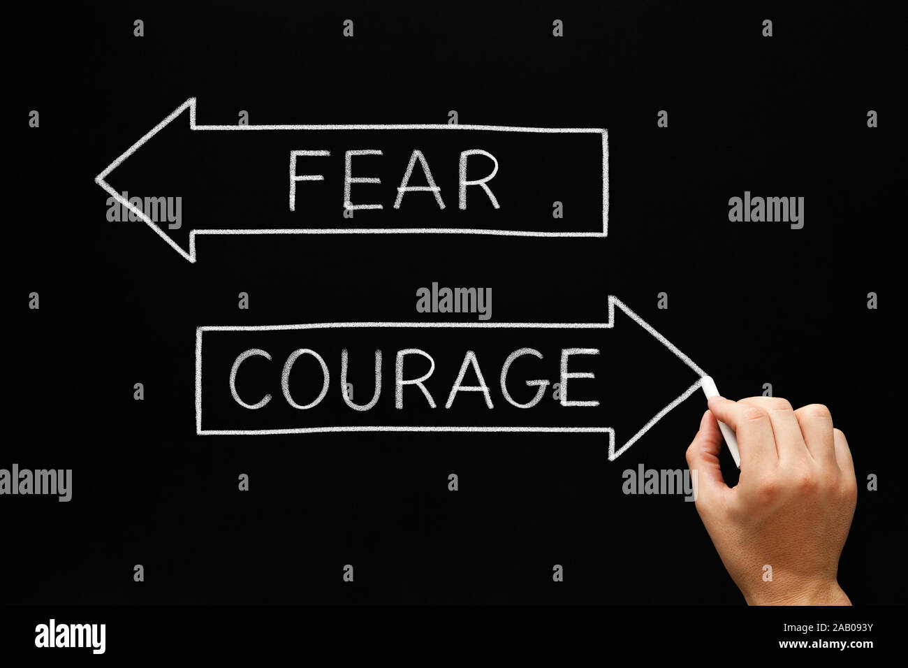 Hand writing the antonym words Courage and Fear on two arrows with white chalk on blackboard. Stock Photo