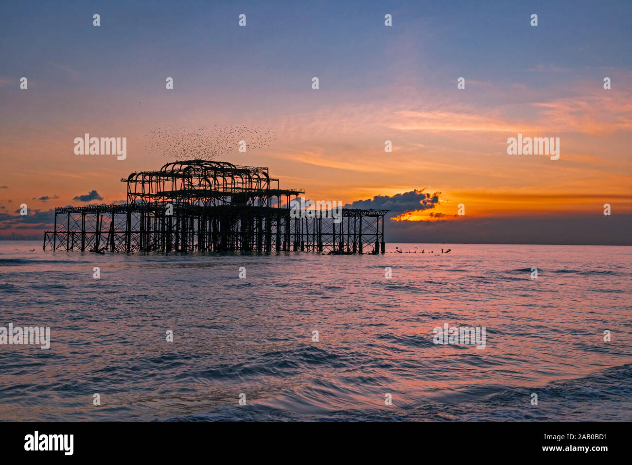 Murmuration over the ruins of Brighton's West Pier on the south coast of England. A flock of starlings swoops over the pier at sunset before roosting. Stock Photo