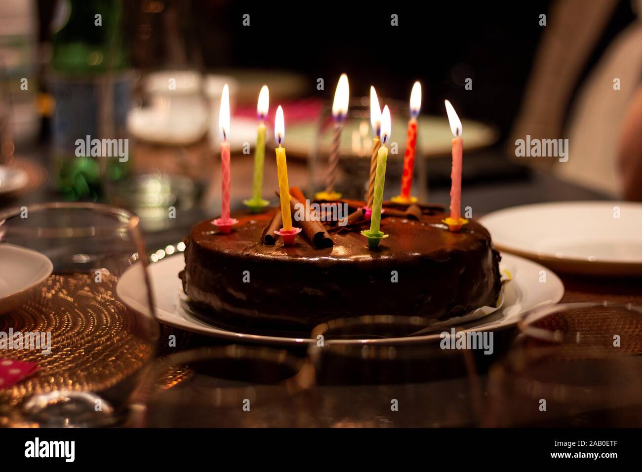 A portrait of a chocolate birthday cake with burning candles on it on a  festive dining table. The lit candles all have different colors Stock Photo  - Alamy