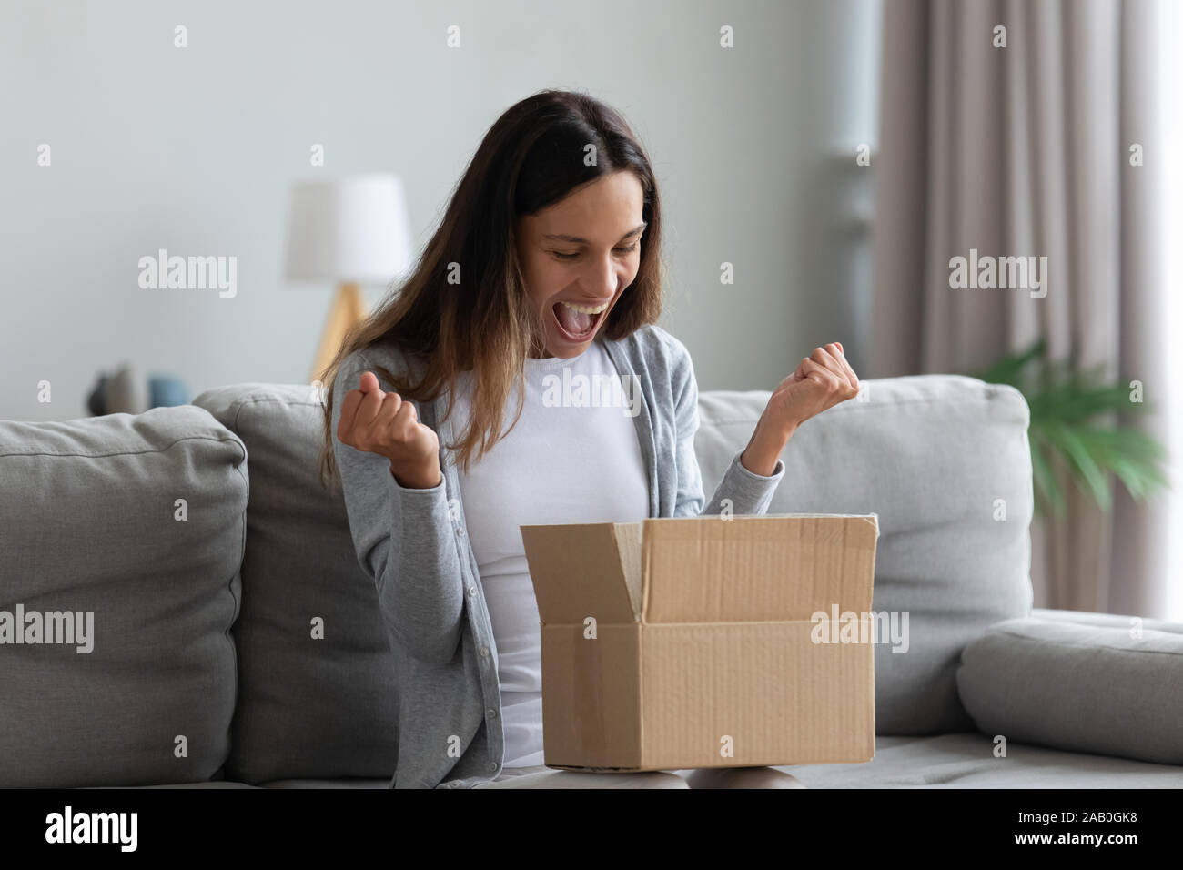 Woman screaming with joy opens carton parcel box feels happy Stock Photo