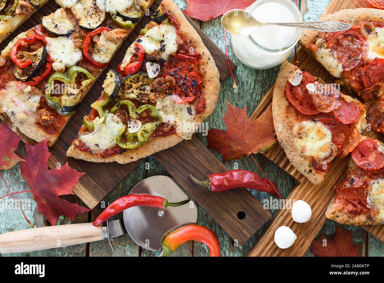 Fall comfort meal. Homemade pizzas with eggplants, peppers, salami and mozarella on oak boards with maple leaves above view Stock Photo