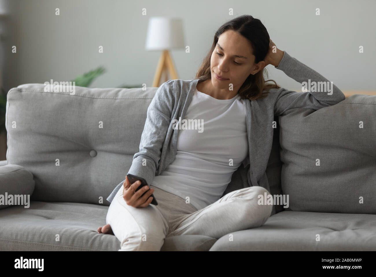 Attractive 30s woman sitting on couch using mobile phone Stock Photo